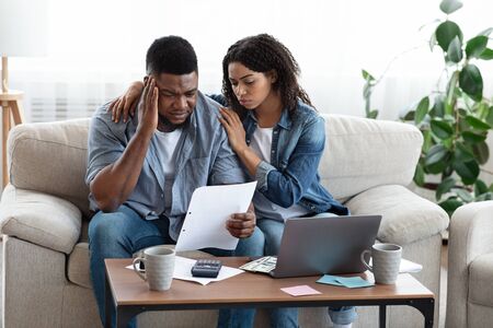 Family Financial Crisis Concept. Depressed Black Couple Looking At Invoice, Not Able To Pay Huge Bills, Suffering From Coronacrisis At Homeの写真素材