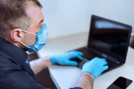 Coronavirus And Business. Mature Entrepreneur Working On Laptop Computer Wearing Gloves And Mask Sitting At Home. Selective Focusの写真素材