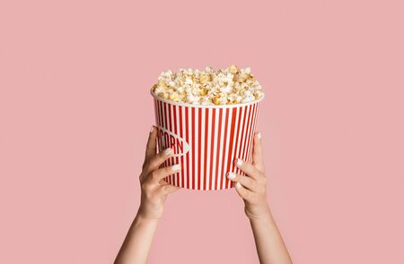 Young girl holding striped bucket with popcorn on pink background, close up viewの写真素材