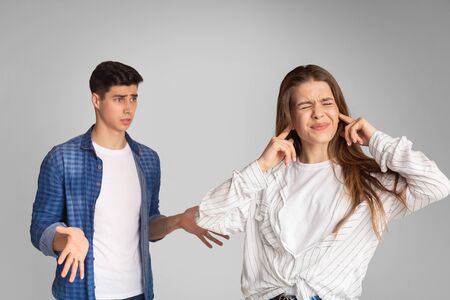 Young couple quarreling, girl covers ears with hands on gray background.の写真素材