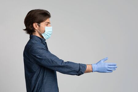 Profile Portrait Of Millennial Man In Medical Mask And Gloves Giving Hand For Handshake Over Light...