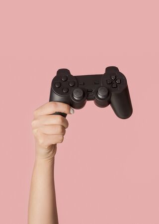 Stay home activities. Female hand showing video game console on pink background, closeup viewの写真素材