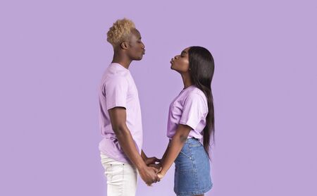 African American boyfriend and girlfriend perking lips for kiss on lilac background