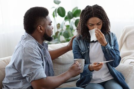 Care And Support. Loving Black Man Caring About His Ill Spouse Suffering From Coronavirus At Home, Offering Her Teaの写真素材