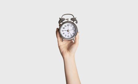 Time optimization concept. Female hand holding alarm clock on light background, close up viewの写真素材