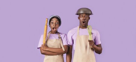 Surprised African American couple with rolling pin and whisk having hard time cooking on lilac background, panoramaの写真素材