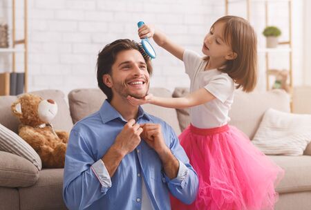 Adorable little girl helping her dad to get ready before job, brushing his hair, home interior, copy spaceの写真素材