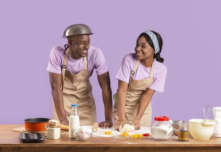 Smiling African American family of two baking cookies together on violet backgroundの写真素材