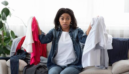 Disorder and mess at home. Shocked young black woman sitting on couch in messy room surrounded by...