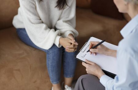Unrecognizable Psychologist Talking With Female Client Taking Notes During Psychotherapy Session...