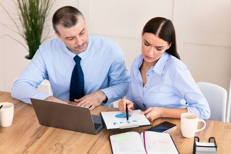 Business Partnership. Two Coworkers Working Together Using Laptop And Charts Sitting At Desk In...