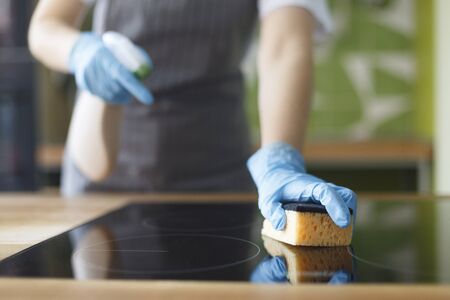 Cleaning before opening. Woman in apron polishing the kitchen worktop with a spray detergent, hygiene concept, blurred backgroundの写真素材