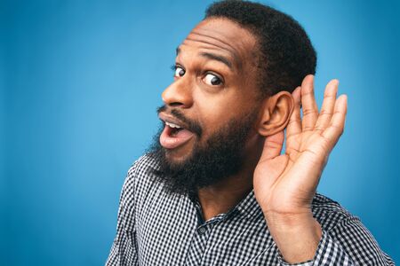 Eavesdropping Concept. Closeup of black guy holding hand near his ear and listening carefully...