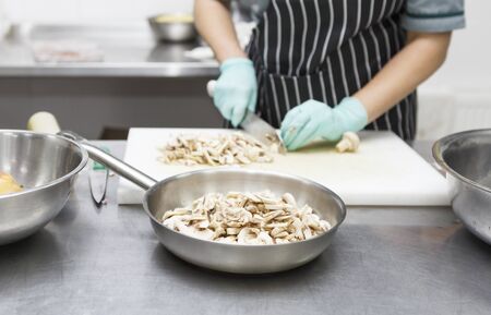 Healthy food concept. Woman in gloves cutting mushrooms for cooking tasty home food for deliveryの写真素材