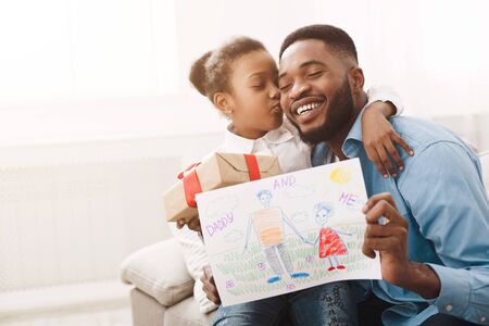 Little black girl hugging father, giving handmade drawing and present box, copy spaceの写真素材