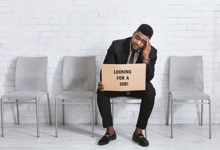 African American man in business suit holding sign LOOKING FOR JOB while waiting for interview in...