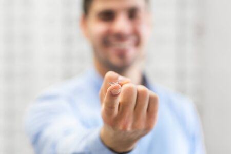 Smiling man holding and showing to camera contact eye lens on finger, copy space, selective focusの写真素材