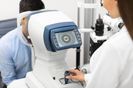 Eye Inspection Concept. Female ophthalmologist checking eye vision of young male customer in modern...