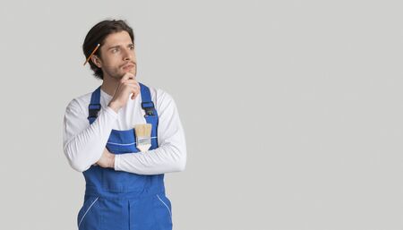 House Renovation Ideas. Portrait Of Pensive Laborer In Work Uniform Touching Chin And Looking Away Deep In His Thoughts, Panorama With Copy Spaceの写真素材