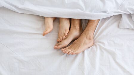 Loving couple in bed. Female and male legs under white blanketの写真素材