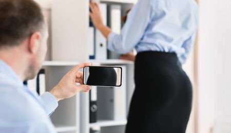 Sexual Harassment At Work. Man Taking Picture Of His Female Coworker's Ass Sitting At Workplace In...