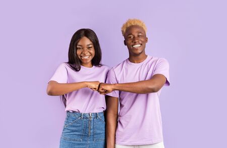 Handsome black guy and lovely girl making fist bump gesture on violet backgroundの写真素材