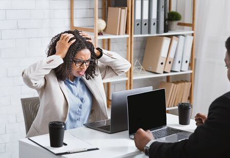 Stressed millennial woman finding mistake, working overtime or missing deadline at officeの写真素材