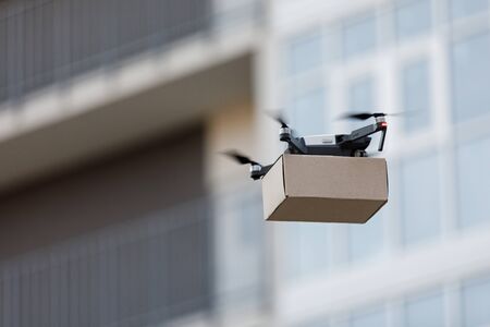 Air robotic worker. Drone carrying cardboard parcel in the air, blurred background, copy spaceの写真素材