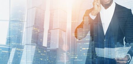 Unrecognizable African American businessman holding documents, double exposure with cityscape at sunrise. Collage with copy space. Panoramaの写真素材