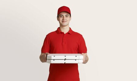 Pizza delivery at home. Smiling courier holds boxes on light background, studio shotの写真素材
