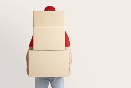Online shopping and package delivery. Courier holds many large parcels, covering face, isolated on light background, studio shotの写真素材