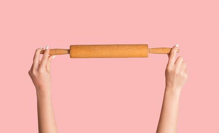 Home baking concept. Woman holding wooden rolling pin on pink background, closeup of hands. Panoramaの写真素材