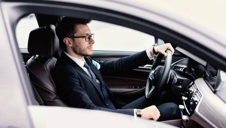 Confident Businessman Concept. Young man in glasses driving in luxury car, side viewの写真素材