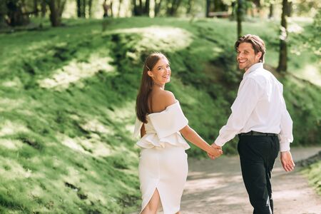 Minimalistic Nature Wedding. Newly-Married Couple Walking In Park Holding Hands Smiling To Camera Celebrating Event Without Guests. Empty Spaceの写真素材