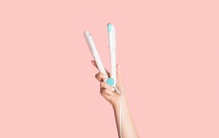 Millennial woman holding hair straightener on pink background, closeup. Panoramaの写真素材
