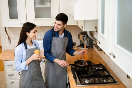 Cooking At Home. Smiling married couple preparing dinner, frying meal on pan, spending time togetherの写真素材