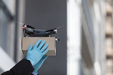 Man in protective gloves receiving quadrocopter with cardboard parcel, safety delivery, copy space