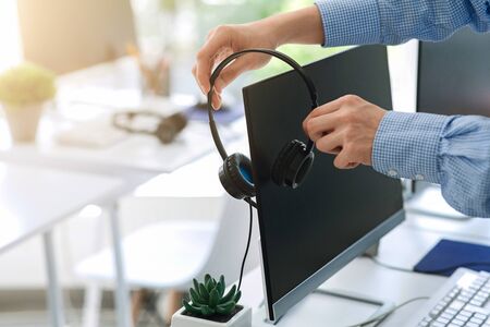 Contact center worker placing his headset on computer monitor at office, close up of hands. Copy...