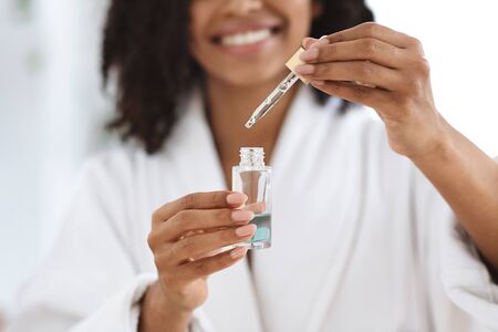Beauty And Skincare. Smiling Black Woman Holding And Opening Bottle With Moisturizing Face Serum,...