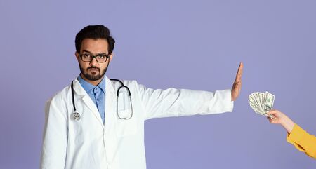 No to corruption concept. Serious Indian doctor refusing bribe from female patient on lilac background, panoramaの写真素材