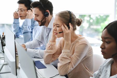 Busy call center assistants with headsets working in front of computer monitors in open space office