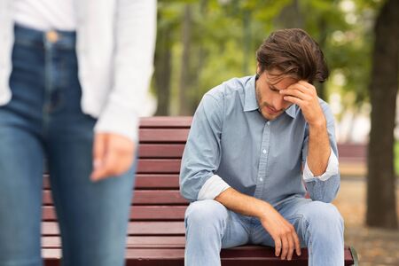 Breakup Concept. Unrecognizable Girlfriend Leaving Sad Boyfriend Sitting On Bench In Park Outside. Cropped, Selective Focusの写真素材