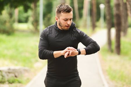 Healthy Lifestyle Concept. Portrait of sporty man running in park, checking his wrist watch, blurred backgroundの写真素材