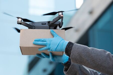 Assembled Drone quadcopter delivering a package and hands in gloves receiving the parcelの写真素材