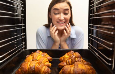 Homemade baking. Glad girl looking at tasty fresh croissants, view from inside of ovenの写真素材
