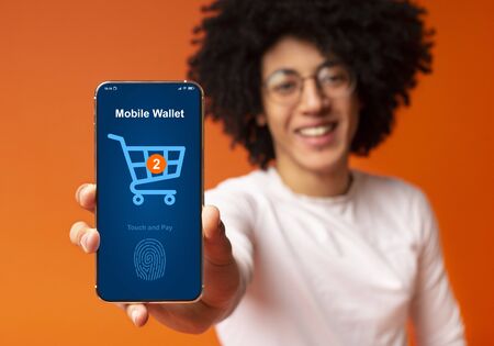 Touch and pay concept. Bushy black guy showing cellphone with online payment form and shopping cart...