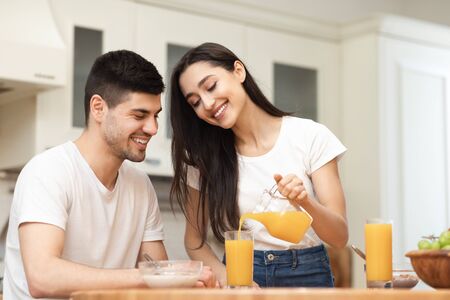Cute european family having breakfast at home in the morning, smiling girl pouring lemonade in glassesの写真素材