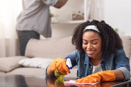 African Couple Making Spring-Cleaning At Home Together, Woman Wiping Table With Rag And Sprayer...