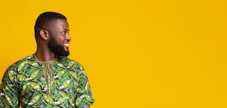 Interested african man in traditional costume looking at copy space over yellow background, panoramaの写真素材