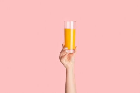 Millennial woman showing glass full of orange juice on pink background, close up. Panoramaの写真素材